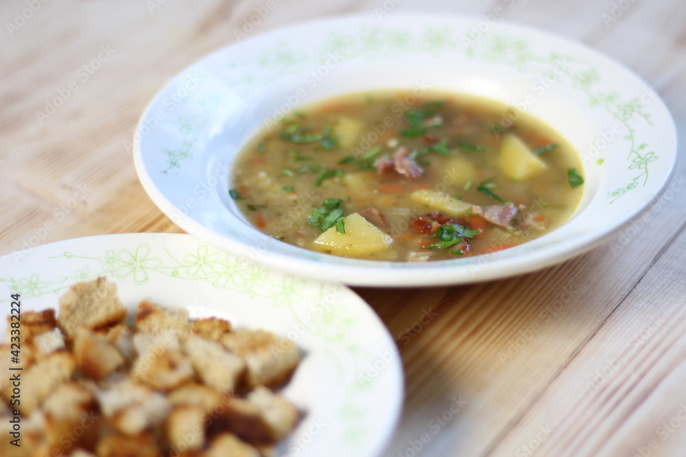 Pea soup with smoked ribs, potato, parsley, toast in rustic bowl on wooden table Pea soup with smoked ribs, potato, parsley, toast in rustic bowl on wooden table