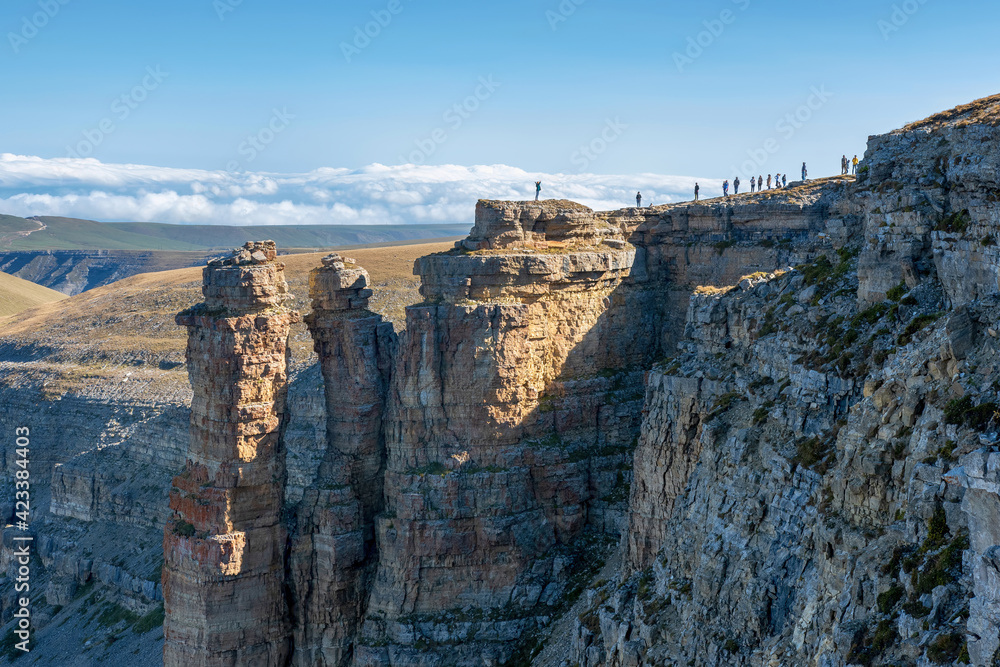 Tourists stand on the edge of Bermamyt plateau on sunny day. Karachay-Cherkessia, Caucasus, Russia.