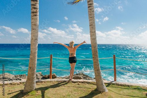 girl stands with her back against the blue ocean between palm trees. Cancun Mexico photo