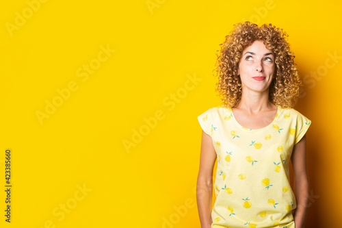 curly young woman pensively looks up on a yellow background