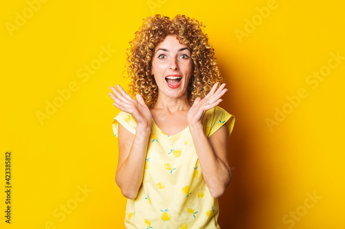 joyful surprised shocked curly young woman on a bright yellow background.