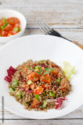 Healthy rustic quinoa salad with vegetables on a white wood table