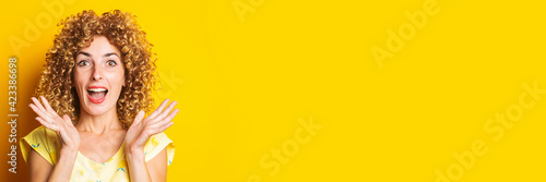 joyful surprised curly young woman on bright yellow background. Banner.