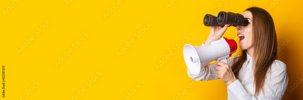 Naklejka premium Friendly young woman holds a megaphone in her hands and looks through binoculars on a yellow background. Hiring concept, help wanted. Banner