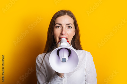 Young woman in a white shirt shouts into a megaphone on a yellow background. Concept for hiring, listing, help wanted. Banner