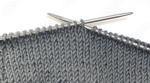 Knitting on knitting needles. Gray woolen fabric on knitting needles on a white background