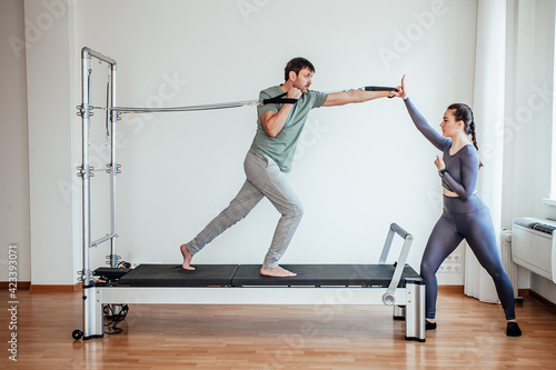 Reformer Pilates.
An attractive man working out with a pilates instructor in the gym
