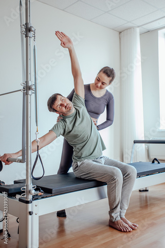 Reformer Pilates. An attractive man working out with a pilates instructor in the gym 