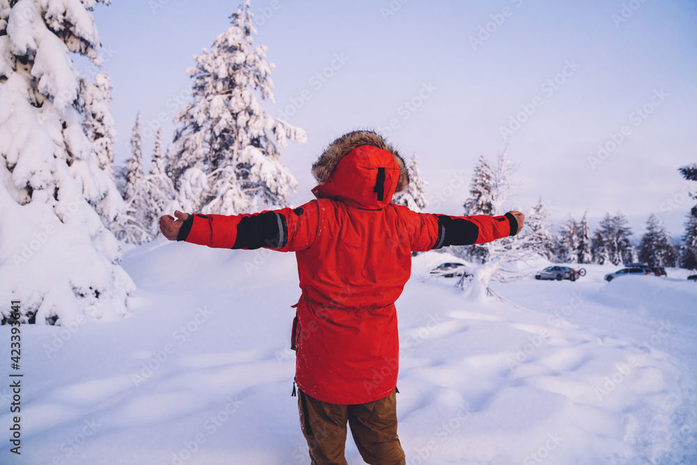 Emotional man traveler standing in winter forest excited with snow and nature, expressive male tourist explore Riisitunturi national park destination raising hands feeeling free