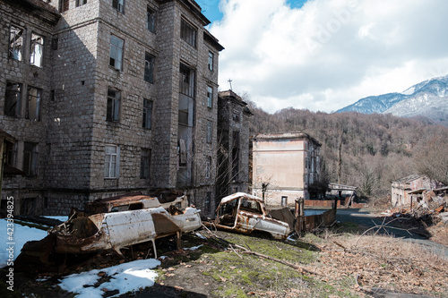 Destroyed abandoned houses after the war in forsaken city, rusty car bodies