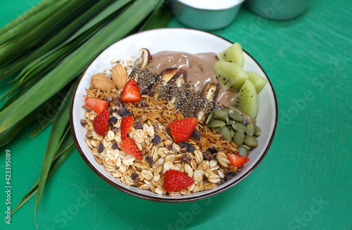 Chocolate smoothie bowl with granola in a coconut bowl on green background, top view. Healthy vegan food concept.                             