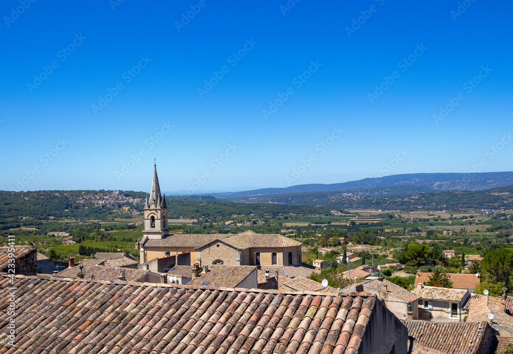 A nice Provencal little village and a church bell tower with a countryside landscape in background by a cloudless sunny day in summer in France