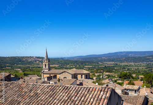 A nice Provencal little village and a church bell tower with a countryside landscape in background by a cloudless sunny day in summer in France