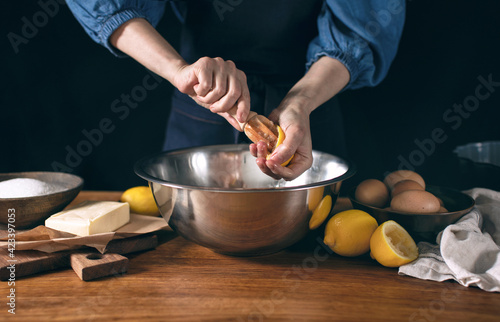Woman wearing dark blue apron cooking lemon cake squeezing the lemon at the moment, front view