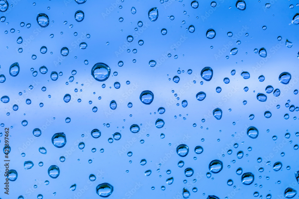 blue rain water drops on a window glass close up , colored drop background macro in a blue light