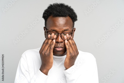 Obraz na płótnie Sleepy African American man wear glasses rubbing his eyes, feels tired after work on laptop computer, isolated on grey background