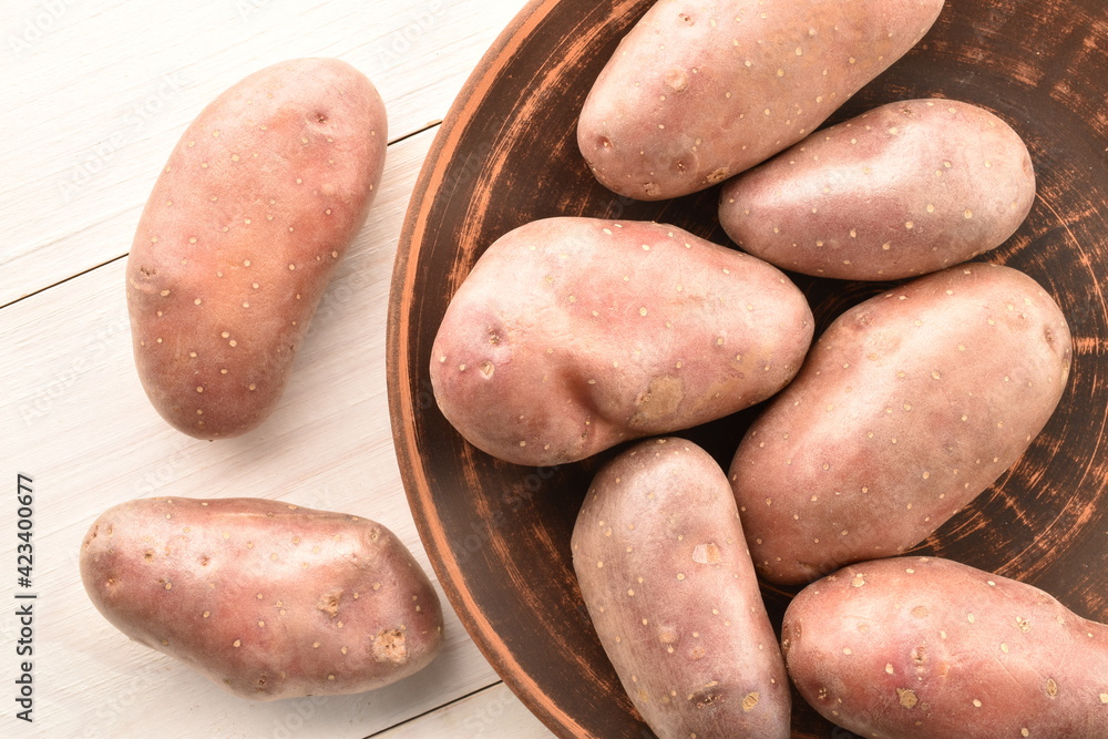 Several unpeeled raw potatoes in a ceramic plate on a wooden table, close-up, top view.