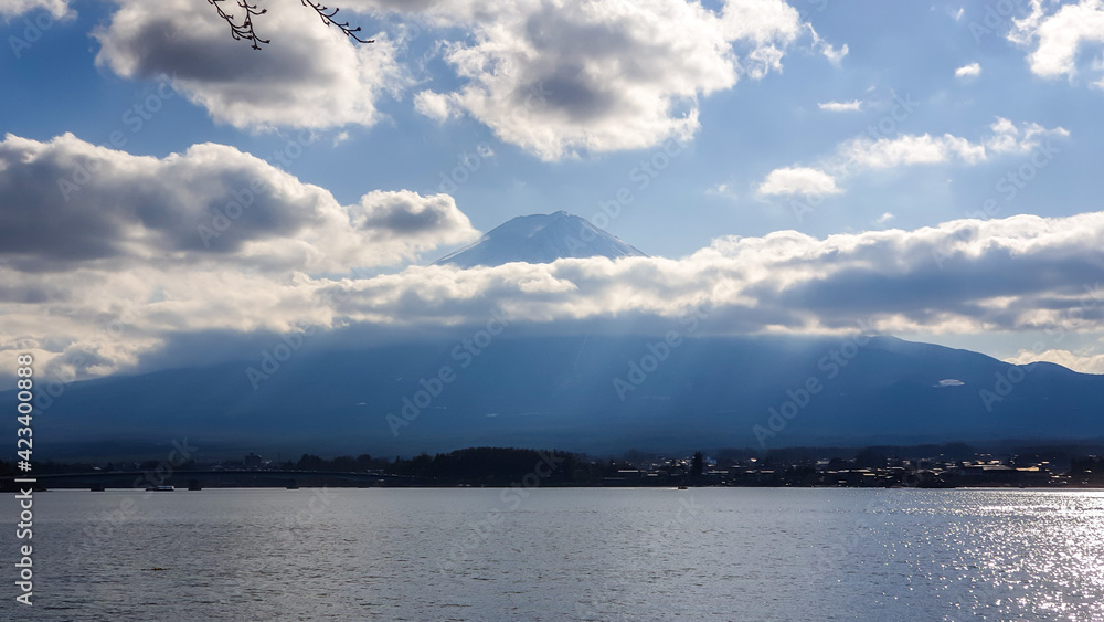 An idyllic view on Mt Fuji from the side of Kawaguchiko Lake, Japan. The mountain is hiding behind the clouds. Top of the volcano covered with a snow layer. Serenity and calmness. Calm lake's surface