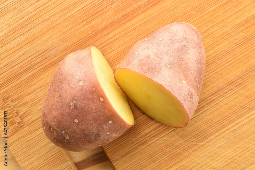 Two halves of unpeeled raw potatoes on a wooden table, close-up, top view. Two halves of unpeeled raw potatoes on a wooden table, close-up, top view.
