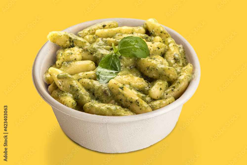 Gnocchi with Genoese pesto sauce in takeaway cardboard plate, isolated on yellow background