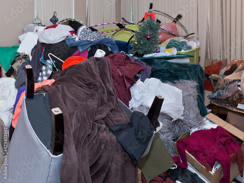 Large Messy Junk Pile. Side view of a large pile of household objects stacked in the middle of a room including a chair, clothes, papers, blankets, bowls, cups, kitchen and Christmas items.