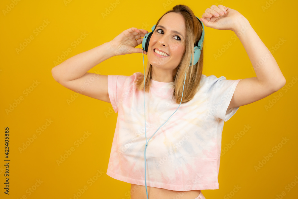 Young pretty woman in headphones smiling broadly isolated over yellow background. Young pretty woman in headphones smiling broadly isolated over yellow background.