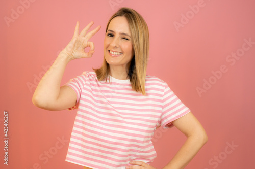 Young beautiful woman wearing summer clothes standing over pink isolated background smiling positive doing okay sign with hand and fingers. Successful expression.