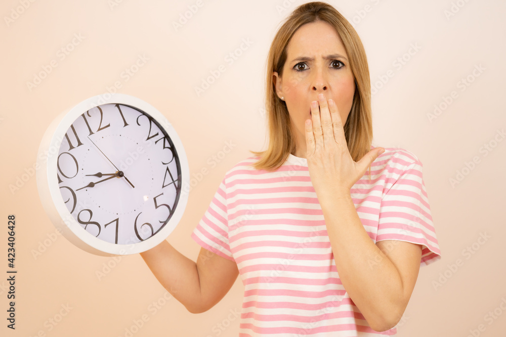 Young surprised woman holding a big clock over white background Young surprised woman holding a big clock over white background