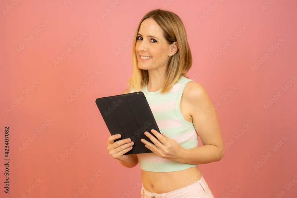 Young attractive smiling woman using a tablet computer over pink background Young attractive smiling woman using a tablet computer over pink background