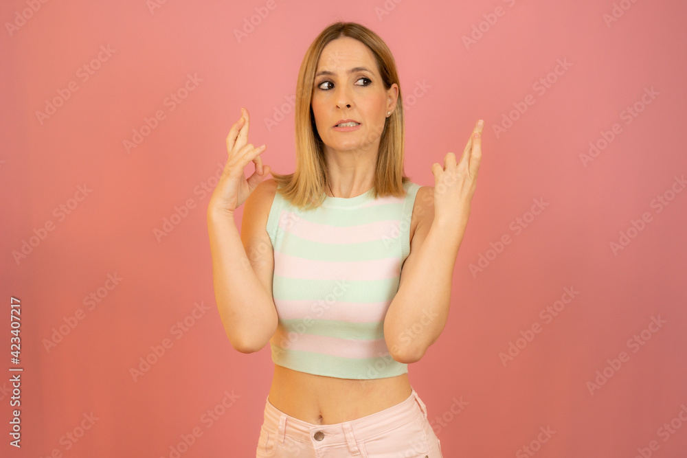 Portrait of a smiling young woman standing over pink background, holding fingers crossed for good luck Portrait of a smiling young woman standing over pink background, holding fingers crossed for good luck