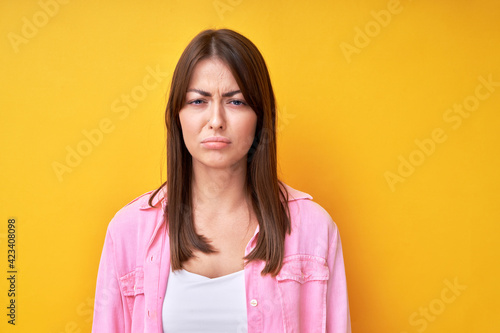 Young brunette woman with offended upset face isolated in yellow studio