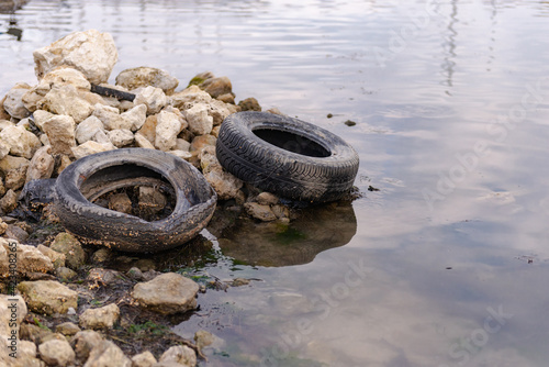 Old tires on the beach. Pollution of the reservoir with old car tires. Garbage on the shore