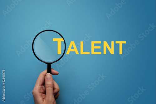 A person with a magnifying glass examines the word - talent. Symbol of the search for talented people