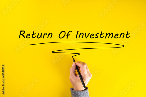 Businessman hand writing return on investment on yellow background. Business Concept