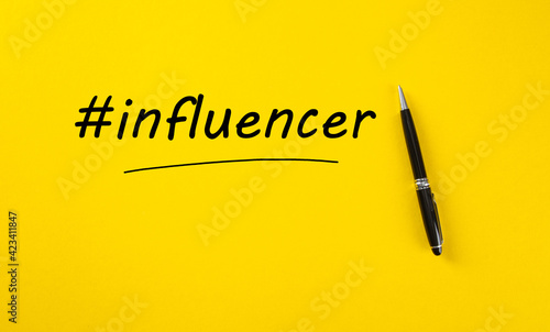Hand written influencer word with hashtag symbol and a pen marker on yellow background. Social media influencer concept.