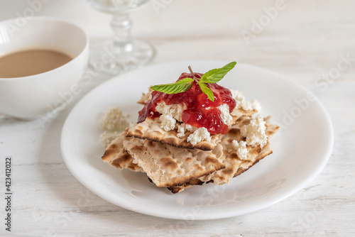 Breakfast ideas for Jewish holiday Pesach. Matzah bread, cottage cheese and strawberry sauce on white plate.