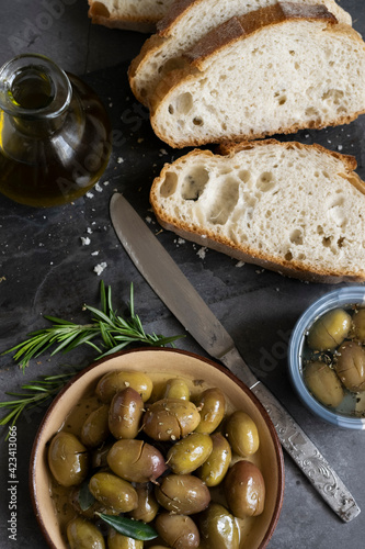 Italian sliced ciabatta bread on chopping board with herbs, extra virgin oil and marinated olives on dark grunge backdrop
