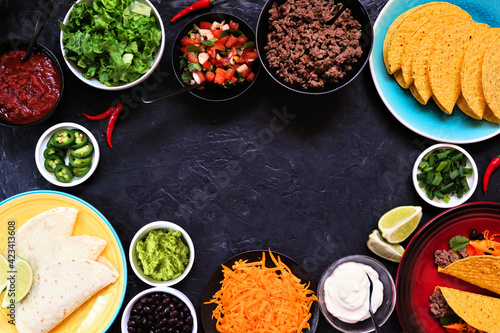 Taco bar frame with assorted ingredients. Above view on a dark slate background. Mexican food buffet. Copy space.