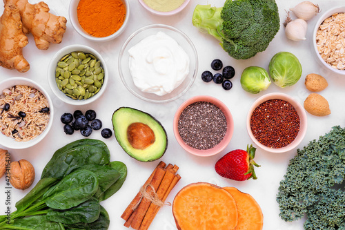Set of healthy food ingredients. Overhead view table scene on a white marble background. Super food concept with green vegetables, berries, whole grains, seeds, spices and nutritious items.