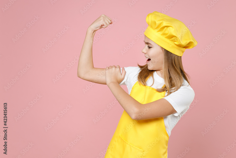 Teen strong sporty girl chef cook confectioner baker housewife in yellow apron white t-shirt cap put arm on biceps muscles on hand demonstrate strength isolated on pink background studio Food concept. Teen strong sporty girl chef cook confectioner baker housewife in yellow apron white t-shirt cap put arm on biceps muscles on hand demonstrate strength isolated on pink background studio Food concept.