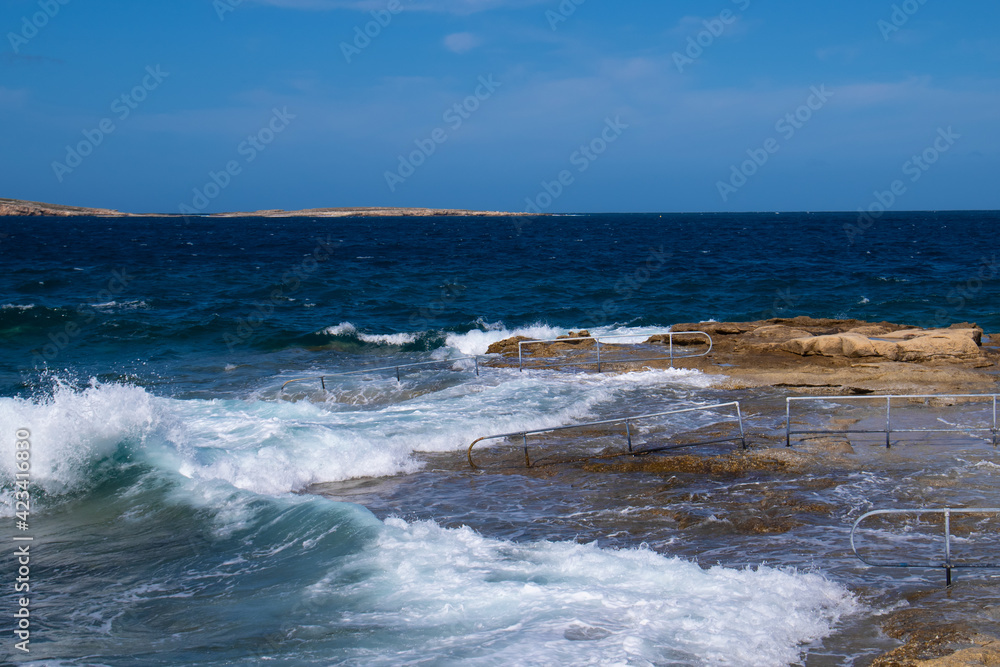 Rocky beach in St Paul's Bay, Malta. Beautiful stormy blue Mediterranean sea. Selective focus.