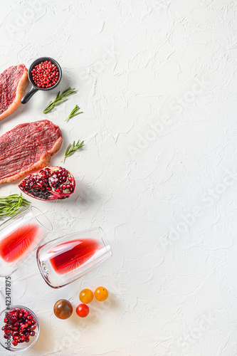 Set of picanha organic beef steaks with rosemary, peppercorns, pomegranate, near red wine in glasses and bottle over white textured  background, top view with space for text.