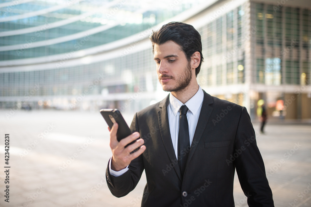 Businessman reading a message on his smartphone outdoor in a modern city setting Businessman reading a message on his smartphone outdoor in a modern city setting
