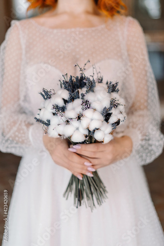 Wedding bouquet of dried lavander and cotton in hands of red haired bride in vintage wedding dress