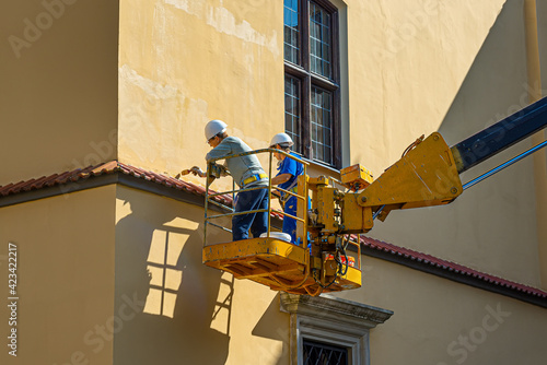 Photography Workers standing on mechanical lift restorer wall of the building