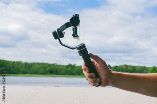 Steadicam with a smartphone in a man's hand. Against the backdrop of the sky and the beach.