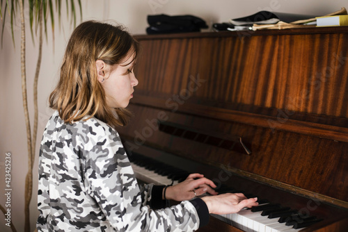 A young teenage girl enthusiastically plays the piano at home, the teacher advises her student on the phone. The girl is preparing for an online piano concert