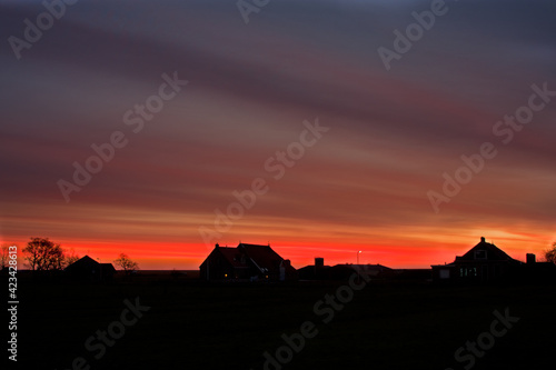 Fiery sky over silhouettes of farmhouses before sunrise on the Dutch island Terschelling photo