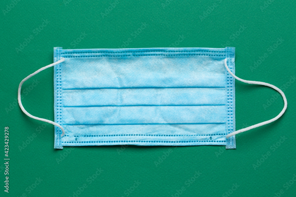 Surgical masks with rubber ear straps on a green background. Typical 3-ply surgical mask to cover the mouth and nose. Procedure mask from bacteria. Surgical masks with rubber ear straps on a green background. Typical 3-ply surgical mask to cover the mouth and nose. Procedure mask from bacteria.