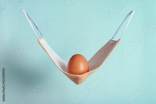 Brown chicken egg with pink fabric medical mask as a hammock
